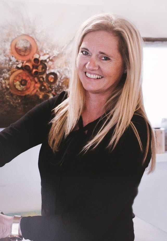 Heidi Douven, zaakvoerder van Kunst voor iedereen, glimlachend voor een van haar werken