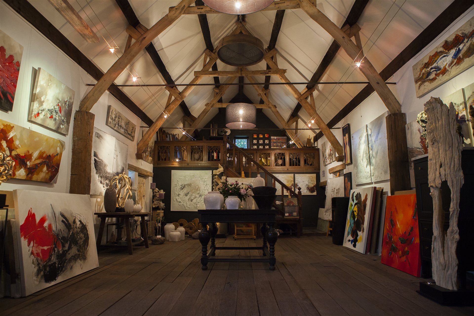 Het sfeervolle interieur van de kunstschuur, met schilderijen langs de houten balken